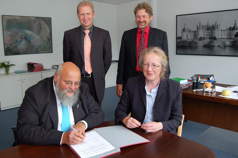Prof. Dr. Katharina Krause (vorne rechts) und Prof. Dr. Marcus Baumann (vorne links) unterzeichnen die Vereinbarung