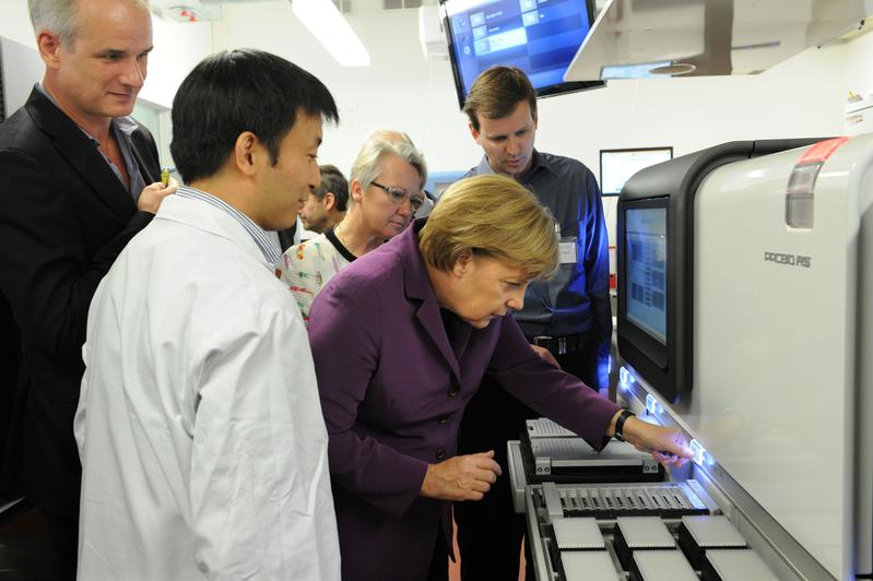 Bundeskanzlerin Angela Merkel startet im Berliner Institut für Medizinische Systembiologie (BIMBS) des Max-Delbrück-Centrums für Molekulare Medizin (MDC) eines der neuesten Sequenziergeräte für DNA-Analysen. Es schauen zu: Dr. Jonas Korlach, Mitentwickler des DNA-Analysegeräts von Pacific Biosciences (r.) und Dr. Wei Chen (vorne), Leiter der Genomikplattform des BIMSB. Korlach ist auch Mitbegründer des Technologieunternehmens in Kalifornien. Im Hintergrund: Bundesforschungsministerin Annette Schavan und Prof. Nikolaus Rajewsky (l.), wissenschaftlicher Leiter des BIMSB. 