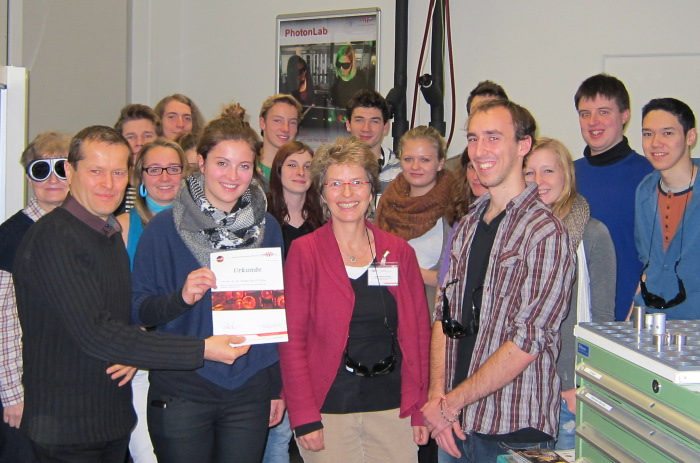 Eine/Einer aus der 13. Klasse der Staatliche Fachober- und Berufsoberschule Technik München ist der 1000. Besucher im PhotonLab. Stellvertretend nehmen die Klassensprecherin und der Klassensprecher den Gutschein aus Prof. Krausz Händen entgegen; v.l.n.r.: Prof. Krausz, die Klassensprecherin, Dr. Stähler-Schöpf und der stellvertretende Klassensprecher. 