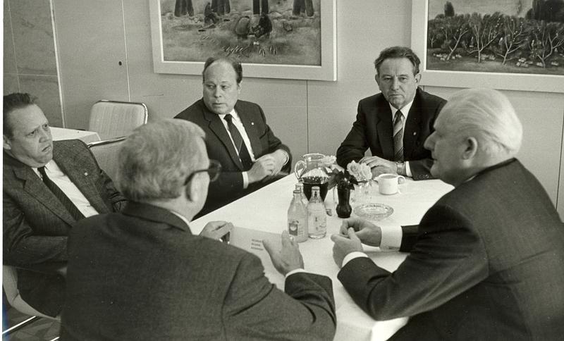 Die Architekten und die Macht. Informelle Gesprächsrunde der Leitung des Bundes der Architekten (BdA) der DDR (Vorsitzender Ewald Henn, hinten) mit den für das Bauwesen entscheidenden Funktionsträgern der SED (Günter Mittag, rechts; Wolfgang Junker, 3.v.l., Günter Schabowski, ganz links) beim 9. Kongress des BdA 1987 im Palast der Republik. 