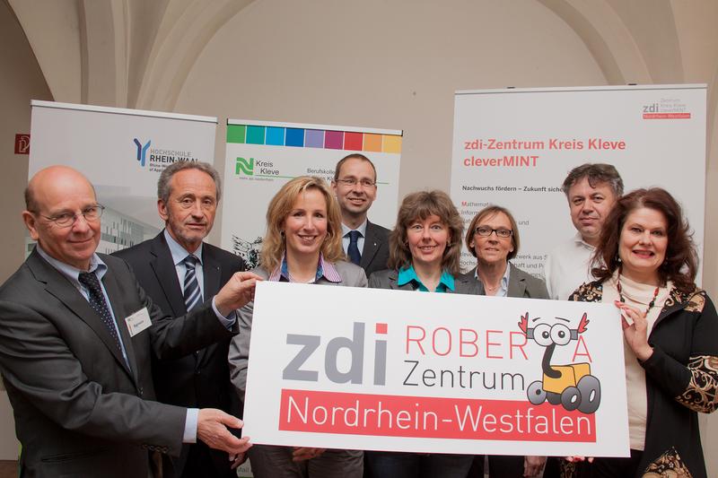 Übergabe des neuen Logos für das zdi-Roberta Zentrum. Personen v.l.n.r.: OStD Thomas Reimers, Schulleiter des Berufskollegs, Dipl.- Ing. Heinz Friedrich Voortmann, Geschäftsführer der Voortmann GmbH & Co. KG Steuerungstechnik, Zandra Boxnick von der Kreisverwaltung Kleve, PD Dr. Gerhard Heusipp, Leiter des Zentrums für Forschung, Innovation und Transfer der Hochschule Rhein-Waal, Ursula Schmitz-Jansen, Leitung des Roberta-Zentrums in Geldern, Martina Bracht-Nienaber, Projektkoordinatorin des zdi-Zentrums des Kreises Kleve cleverMINT, Marius Galuschka von LEGO Education Europe und Brigitte Timmer, Vertreterin des Ministeriums für Innovation, Wissenschaft und Forschung des Landes Nordrhein-Westfalens (MIWF)