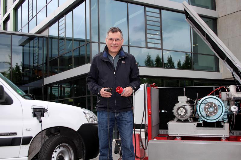 Als „technischer Moderator“ will Thomas Krause (M.) von der Westfälischen Hochschule (im Hintergrund) Überschuss-Strom aus Blockheizkraftwerken (r.) in die Speicher von Elektrofahrzeugen (l.) ableiten. Zwar bleibt ein Stromkabel der technische Übertragungsweg, eine Smartphone-App soll aber schon vorher den technischen Dialog zwischen dem Erzeuger „Gebäudetechnik“ und dem Verbraucher „Auto“ aufbauen.