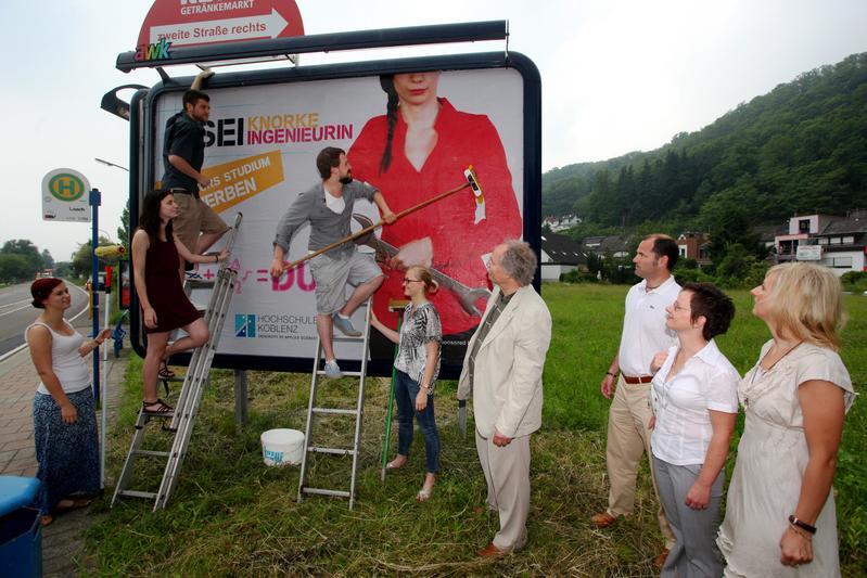Die fünf Marketing-Studierenden bekleben die erste Großfläche mit ihrem Gewinnermotiv im Beisein von Prof. Dr. Kristian Bosselmann-Cyran (Präsident Hochschule Koblenz), Prof. Dr. Holger J. Schmidt (Marketing-Professor im Fachbereich Wirtschaftswissenschaften), Christiane Gandner (Pressesprecherin Hochschule Koblenz) und Stefanie Probstfeld (Leiterin Unternehmenskommunikation der awk AUSSENWERBUNG GmbH).