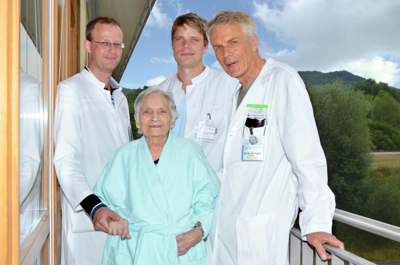 Prof. Dr. Rainer Figulla (Direktor Kardiologie, rechts), Oberarzt Dr. Alexander Lauten (Oberarzt Kardiologie, 2.v.r.) und Herzchirurgie-Oberarzt Dr. Tim Sandhaus (links) mit ihrer gemeinsamen Patientin kurz nach dem Einsatz der neuen Herzklappe am Universitätsklinikum Jena. 