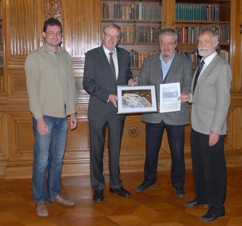 Dr. Dennis Roedder, Dr. Uwe Schäkel, Prof. em. Dr. Wolfgang Böhme und Prof. Dr. Wolfgang Wägele (vlnr) mit einem Sonderdruck der Veröffentlichung und einem Foto der Echse Darevskia schaekeli.