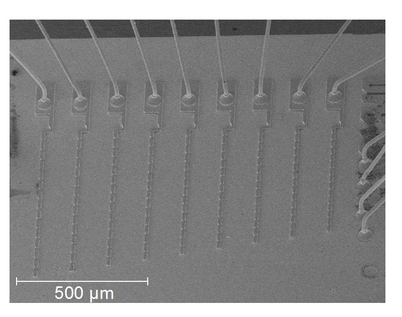 Chip mit neun Terahertz-Quantenkaskadenlasern mit unterschiedlichen Gitterperioden. Im oberen und rechten Teil der Abbildung sind die Golddrähtchen, durch die die Laser elektrisch kontaktiert werden.