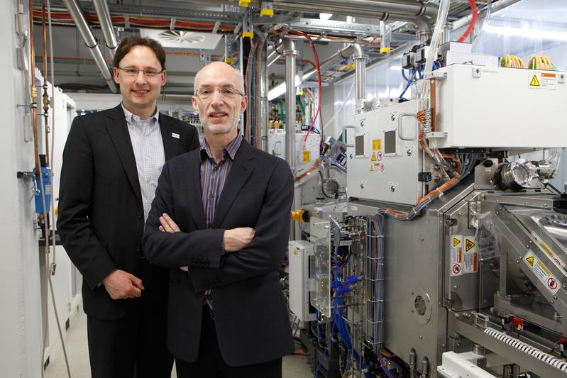 Univ.-Prof. Dr. Mathias Kläui (links) und Prof. Dr. Stuart Parkin (rechts) vor der neuen Industrie-Depositionsanlage Rotaris an der Johannes Gutenberg-Universität Mainz.