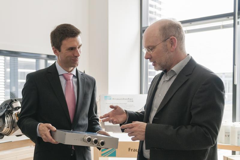Der stellvertretende IISB-Institutsleiter Prof. Dr. Martin März (rechts) informiert Staatssekretär Stefan Müller über die Leistungsfähigkeit moderner leistungselektronischer Wandler. 