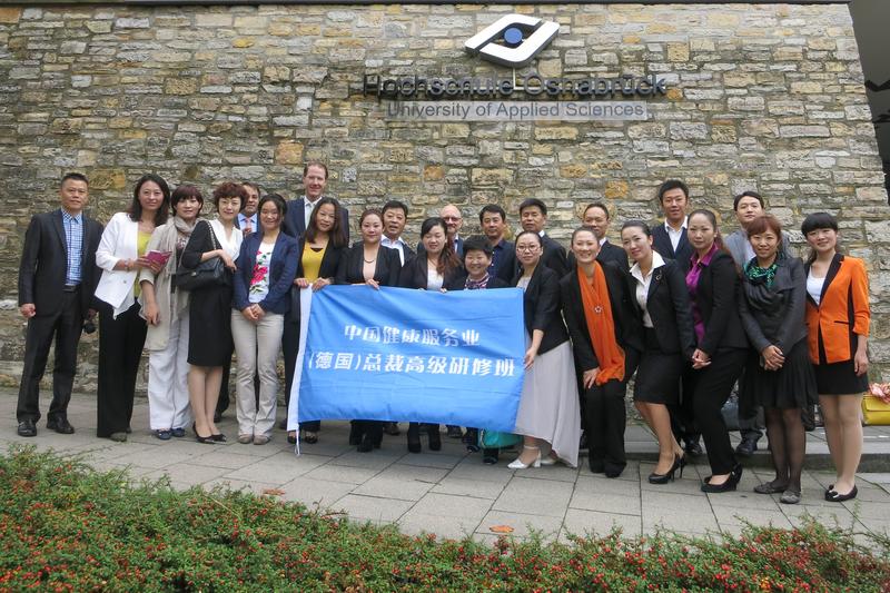 „Weiterbildung im Gesundheitswesen für chinesische Führungskräfte“ steht in chinesischer Schrift auf dem blauen Banner, das die ersten Teilnehmer des neuen Programms in den Händen halten.