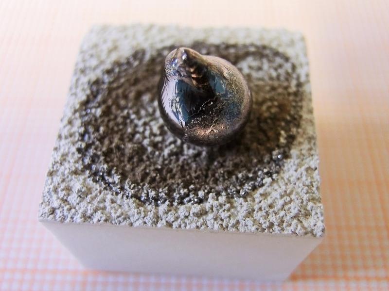 Erstarrter Siliziumtropfen auf einem beschichteten Tiegelstück, Abmessungen 2 cm x 2 cm.