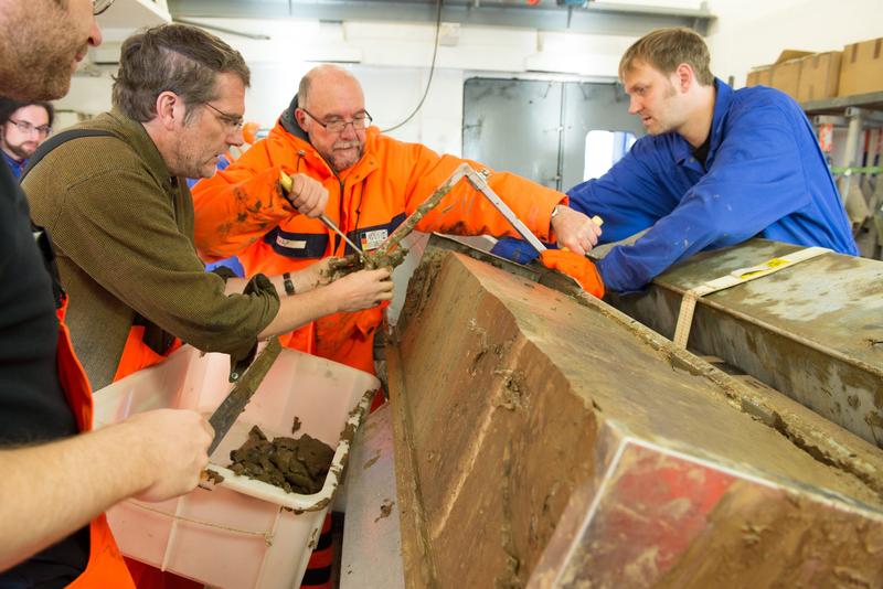 Polarsternfahrtleiter Prof. Dr. Rüdiger Stein (Mitte, orangefarbene Kleidung) und sein Team begutachten im Polarstern-Labor den am Lomonossow-Rücken geborgenen Sedimentkern.