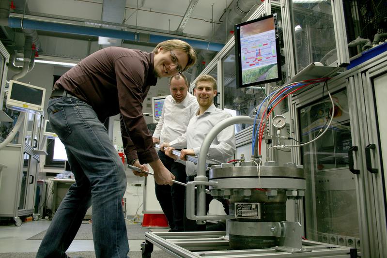 V.l.n.r.: Dr. Ulrich Rost, Jeffrey Roth und Pit Podleschny zeigen auf der Hannover-Messe die Teckenik eines Hochdruck-Elektrolyseur-Prototyps (rechts unten).