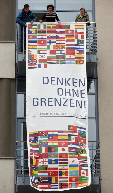 Gemeinsam mit der Vizepräsidentin Prof. Dr. Iris Winkler enthüllen der chinesische Doktorand Tinghui Duan (l.) und die Auslandsgermanistikstudentin Marie Möckel (r.) eines der Banner an der Uni Jena.