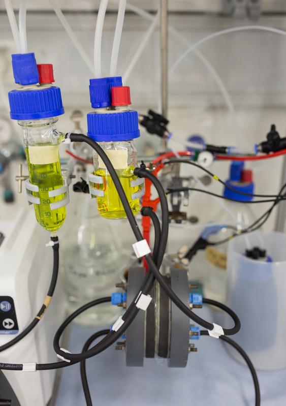 Lab set-up of a redox flow battery with the hydrophobic membrane (grey device at the bottom of the image) and two electrolyte reservoirs (bottles with yellow liquid).