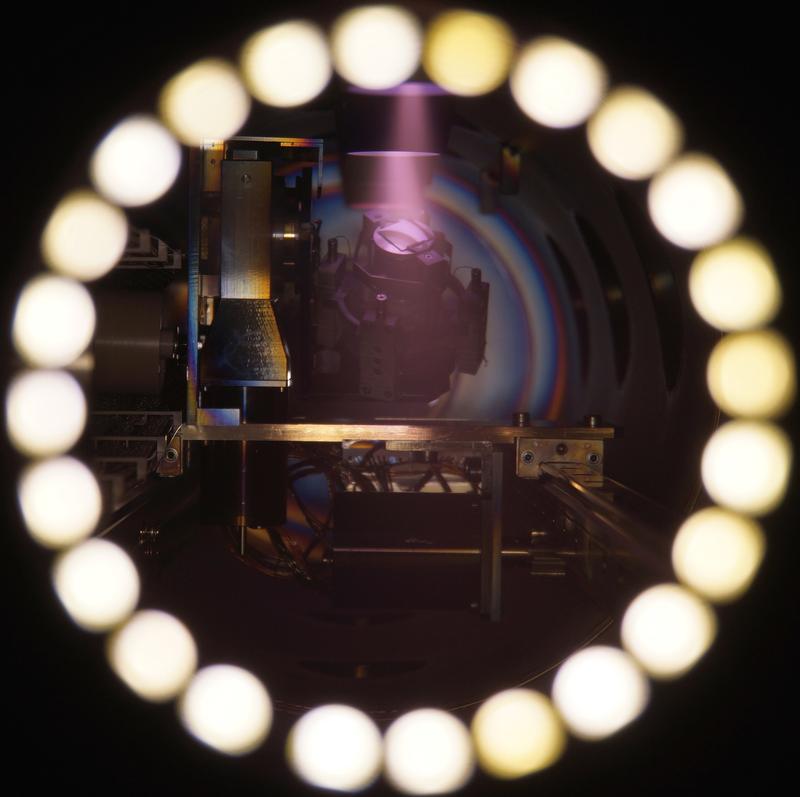 Blick in die Vakuumanlage zur Herstellung der Sensorschichtsysteme. Das Schichtsubstrat befindet sich auf einer Drehhalterung, der Beschichtungsprozess wird durch ein lilafarbenes Plasma sichtbar. 