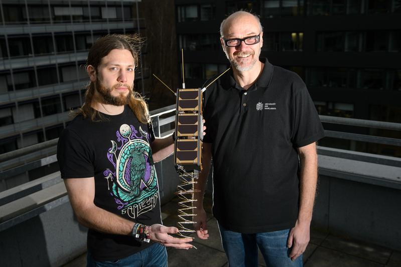 Gilles Nies und Professor Holger Hermanns mit dem Nachbau eines Nano-Satelliten, dessen Leistungsfähigkeit nun mit ihrer Hilfe garantiert werden kann. 
