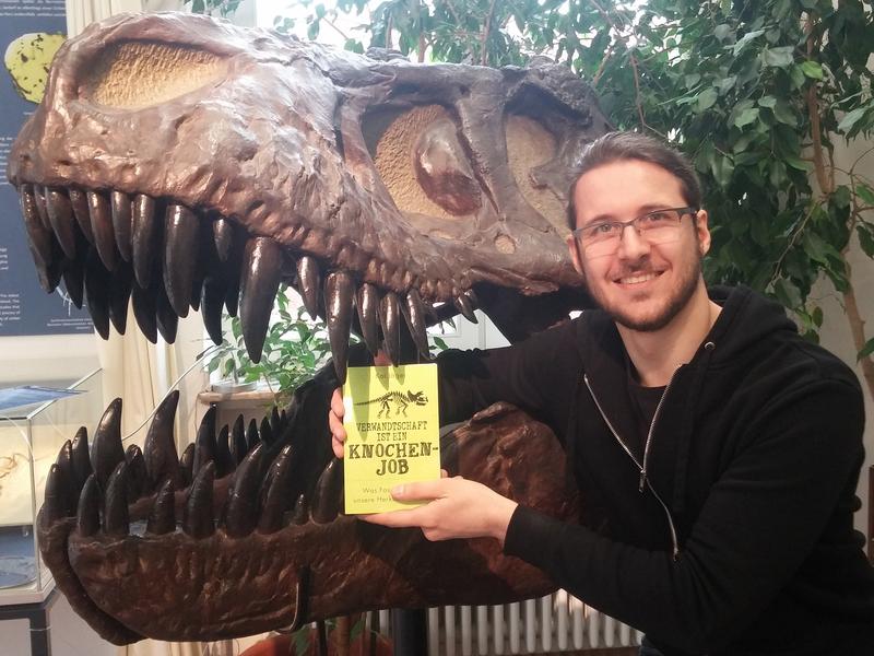 Kai Jäger vom Steinmann-Institut der Universität Bonn mit seinem Buch „Verwandtschaft ist ein Knochenjob“ vor einem Tyrannosaurus rex. 