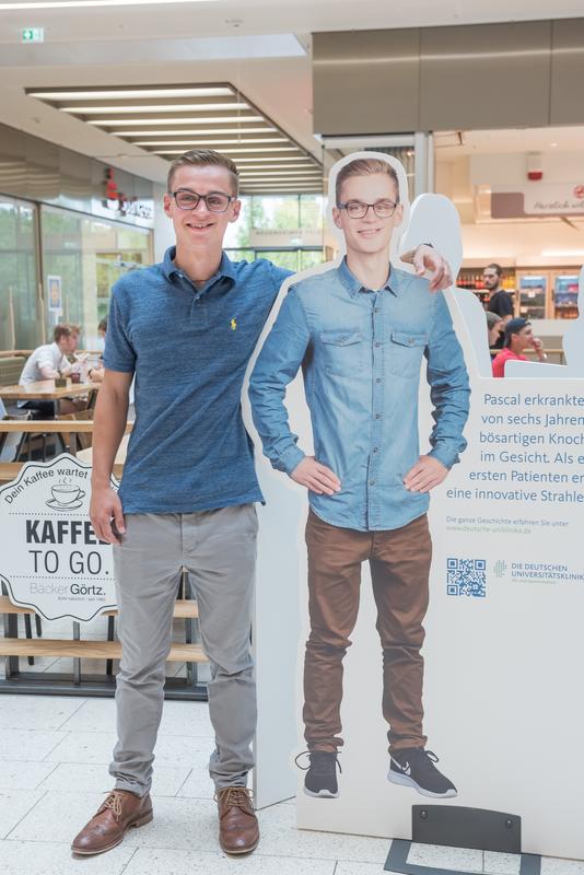 „Dank der Therapie kann ich heute ein ganz normales Leben führen“: Pascal präsentiert seinen Aufsteller der Ausstellung „33 Storys – eine Spitzenmedizin“.