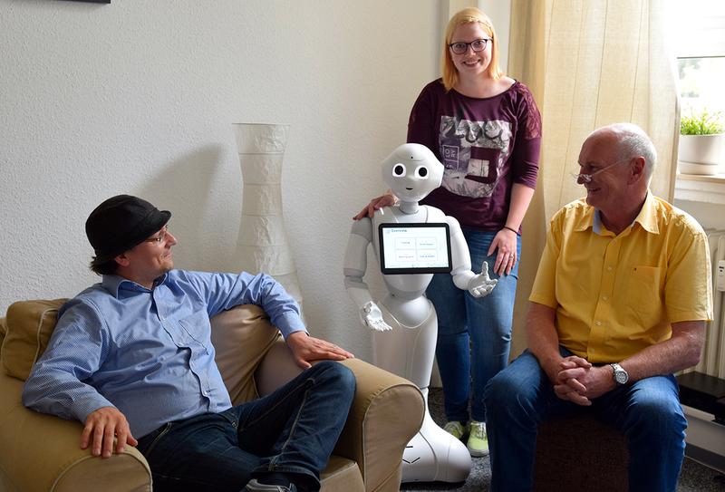 Sebastian Hofheinz, Studentin Jennifer Blazejak und Dr. Rainer Wieching zusammen mit Pepper im Forschungswohnzimmer (v.l.)