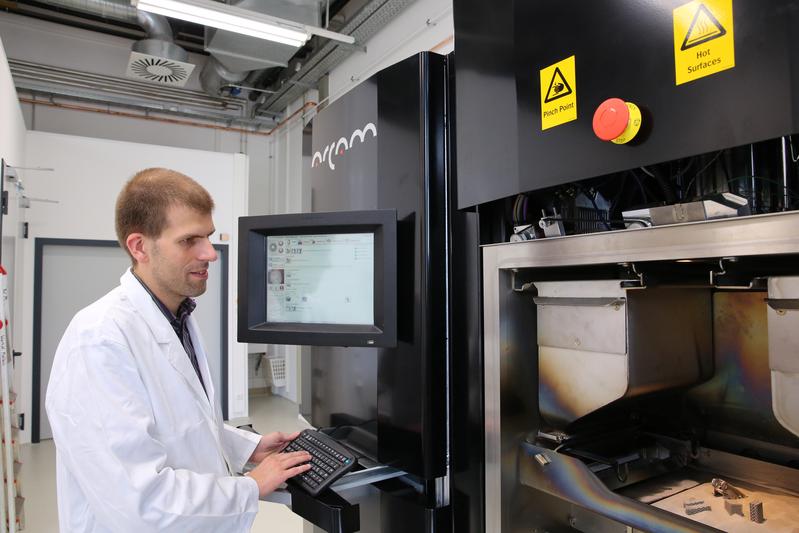 Prof. Dr. Thomas Niendorf mit einem 3D-Metalldrucker (und älteren Produkten).