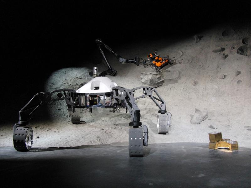 Die am Weltraumszenario beteiligten mobilen Systeme SherpaTT (links), Coyote III (hinten im Krater) sowie ein BaseCamp mit Nutzlastmodul (rechts)