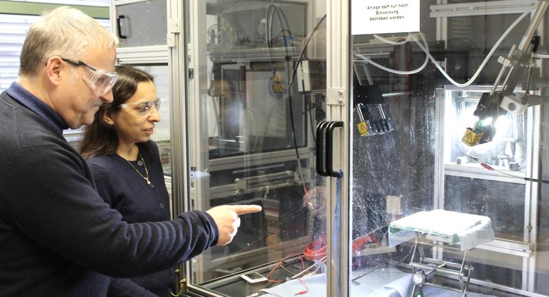 Prof. Dr. Andreas Greiner und Prof. Dr. Seema Agarwal (v.l.) an einer Anlage zum Elektrospinnen. Im Gegenlicht sind die dünnen Fasern zu erkennen, aus denen die Vliesstoffe gebildet werden.