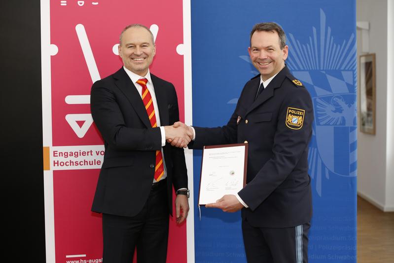 Prof. Dr. Gordon Thomas Rohrmair, Präsident der Hochschule Augsburg, und Michael Schwald, Präsident des Polizeipräsidiums Schwaben Nord, besiegeln die Kooperationsvereinbarung.