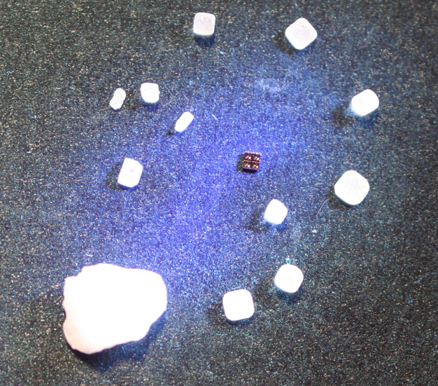 Ein Halbleiter-Chip bestehend aus 4 vertikal emittierenden Laserdioden (VCSEL) im Größenvergleich mit normalen Salzkörnern sowie dem Salzkorn einer Brezel.