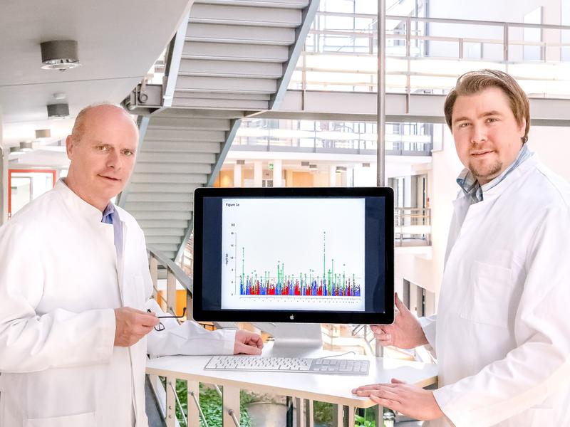 Prof. Dr. Markus Nöthen (links) und Dr. Andreas Forstner  mit einem Manhattan-Diagramm: Die assoziierten Stellen im menschlichen Genom ragen als "Skyscraper" aus dem Hintergrundrauschen heraus. 