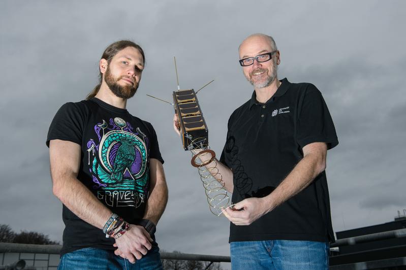 Gilles Nies (l.) und Professor Holger Hermanns mit dem Satelliten, dessen Mission sie mit neuen Rechenmodellen absichern.