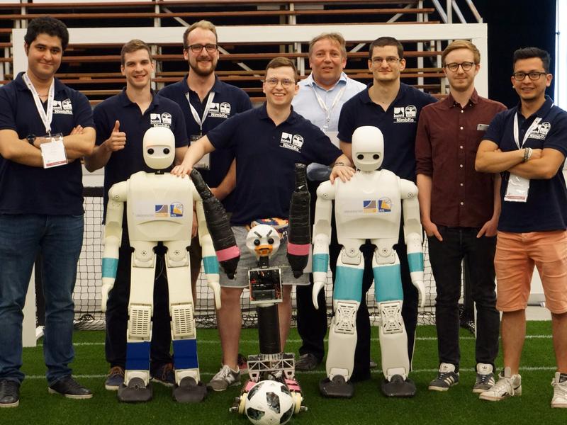 Siegreich: Prof. Dr. Sven Behnke (letzte Reihe Mitte) mit seinem Team NimbRo von der Universität Bonn. Im Vordergrund stehen zwei Roboter der AdultSize-Klasse. 