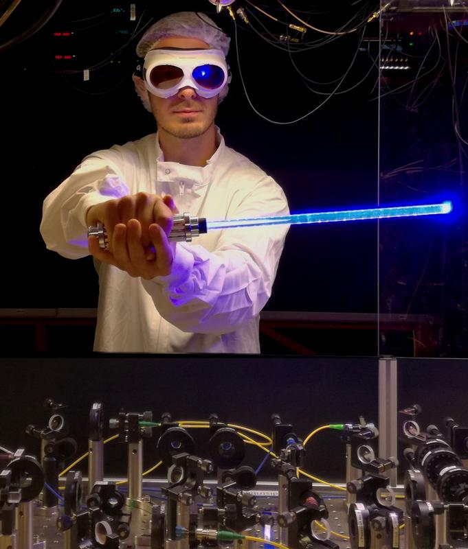 Doktorand Nicolas Tolazzi vor dem Experiment, in der Hand ein Spielzeug-Lichtschwert. 