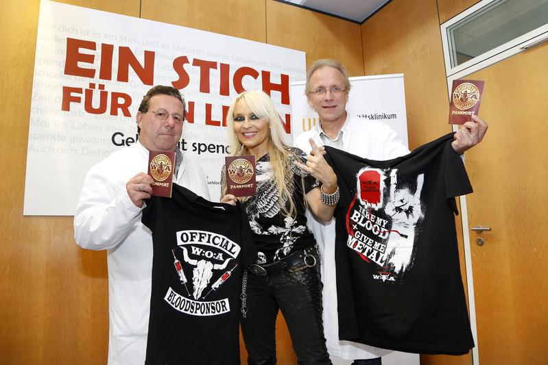 Doro Pesch und die Dr. Erik Lehnert (li.) und Dr. Johannes Fischer vom UKD präsentieren das offizielle „Wacken-Blood-Sponsor-T-Shirt“, dass es für sechs Blutspenden an der Uniklinik Düsseldorf gibt. 