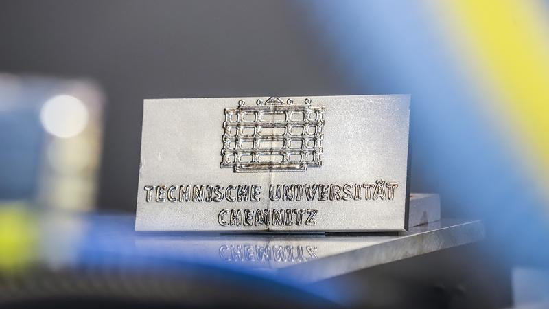 Besonderer Werkstoffverbund: Mittels Laserauftragschweißen kann beispielsweise auch das Logo der TU Chemnitz in Szene gesetzt werden, indem metallisches Glas auf Edelstahl aufgetragen wird.