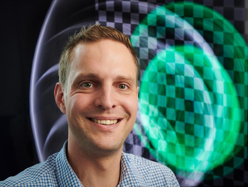 Professor Matthias Hullin von der Universität Bonn. Der Hintergrund zeigt ein optisches Echo, das mit in Bonn entwickelten Verfahren simuliert wurde. 