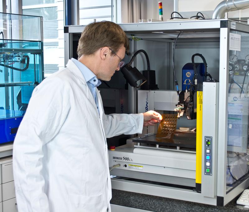 Dr. Roman Tkachov begutachtet an einem Dispensdrucker im Fraunhofer IWS Dresden eine Folie, die er mit zwei verschiedenen leitenden Polymeren bedruckt hat.