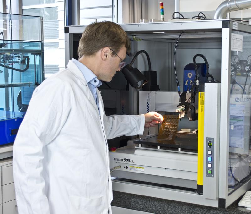 Dr. Roman Tkachov examines a film printed with two different conductive polymers at a dispensing printer in the Fraunhofer IWS Dresden. 