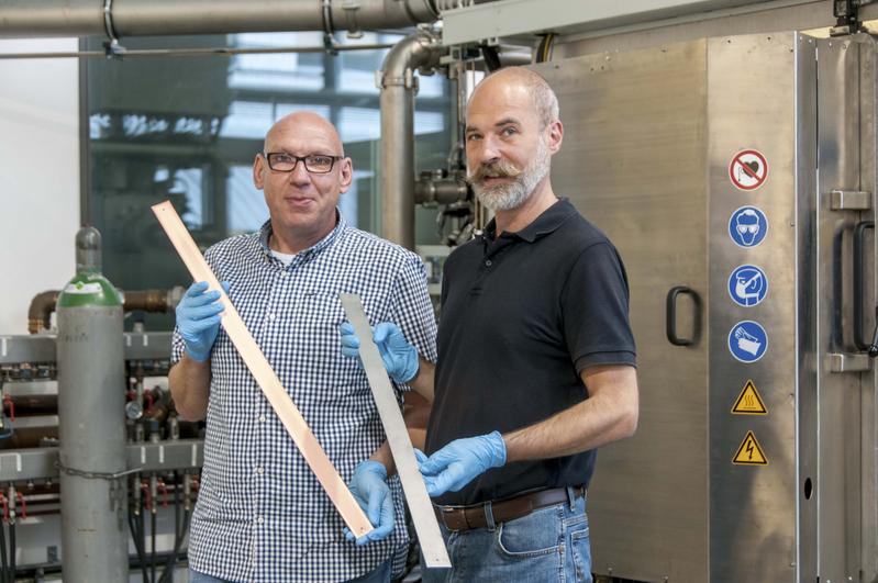 Die Entwicklungsingenieure des IST vor der Beschichtungsanlage: Ralf Wittorf (links) mit einem kupferbeschichteten Muster aus Titan, daneben Torsten Hochsattel mit dem unbehandelten Probenmaterial.