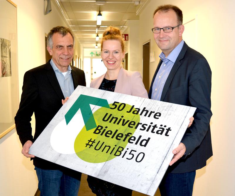 Rektor Prof. Dr.-Ing. Gerhard Sagerer, Projektleiterin Dr. Sarina Bornkessel und Martin Knabenreich (Bielefeld Marketing) (v.l.n.r.) mit dem neuen Jubiläumslogo.