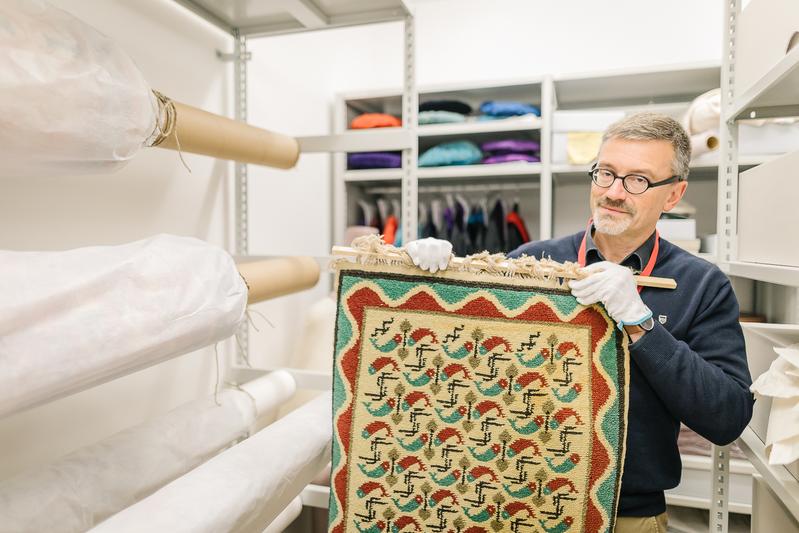 Curator of the University of Greifswald, Dr. Thilo Habel, holding a Pomeranian Fischerteppich by Rudolf Stundl in the storeroom