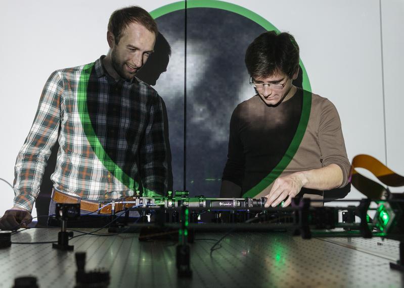 Sergey Turtaev (on the left) and Ivo T. Leite from Leibniz-IPHT. The projection behind them shows an image of neurons obtained deep inside the brain via a single multimode fibre. 