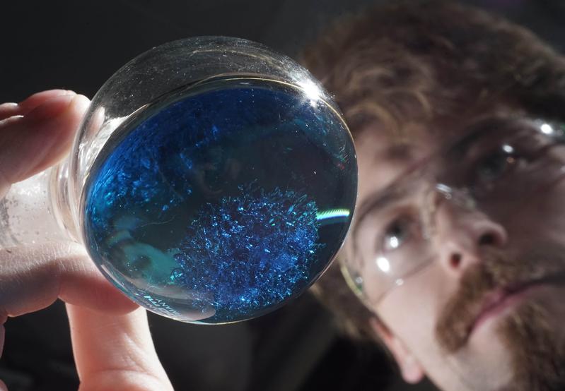 Der Jenaer Doktorand Benjamin Kintzel betrachtet ein Laborgefäß mit Kristallen eines neuartigen Moleküls, das möglicherweise in einem Quantencomputer Verwendung finden kann. 