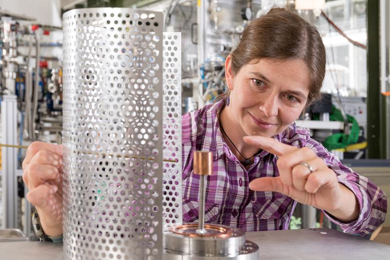 Dr. Eve Stenson uses spare parts to demonstrate the structure of the positron trap. In the prototype trap, the magnetic field is generated by a permanent magnet (center).