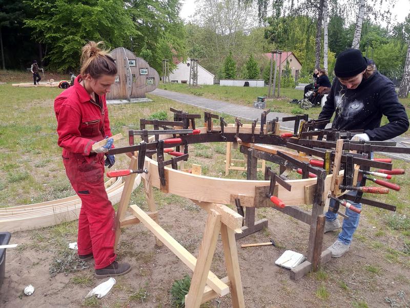 Workshop-Teilnehmerinnen Anne Geyersbach (links) und Schirin Steinhauer kleben die unter Wasserdampf gebogenen Eschenbretter zum Dachkranz zusammen.