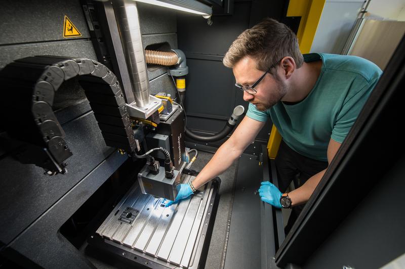 Doktorand Daniel Müller legt ein Werkstück in die neue Anlage für Laserinterferenz-Technologie.