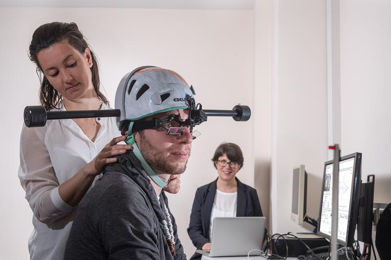 Dr. Cecilia Ramaioli (left) checks if the weighted helmet fits correctly to the head of a study participant. In the background, Prof. Nadine Lehnen prepares the computer for the experiment. 