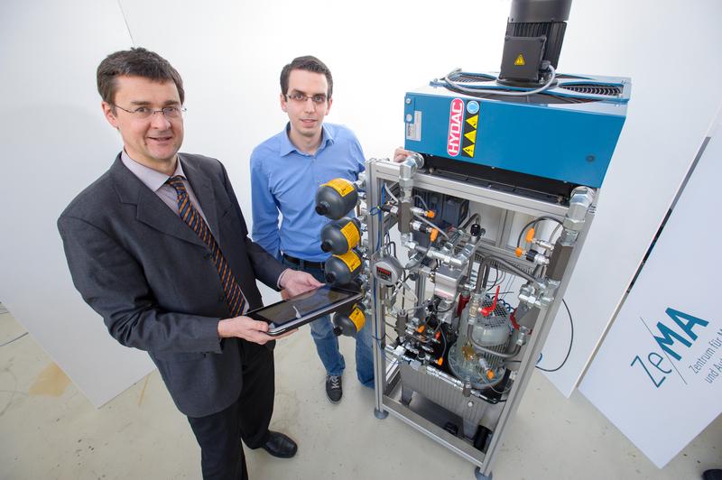 Ein Sensorsystem beobachtet die Maschine und warnt, wenn sich ein Schaden ankündigt: Prof. Andreas Schütze (l.) und Nikolai Helwig zeigen das Verfahren mit einem Hydraulik-Teststand.