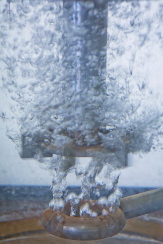 Detailaufnahme aus dem Reaktor: Unten ein Gasverteiler mit Luftblasen, oben ein Rührer