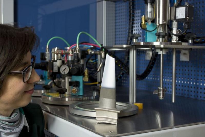 Dr. Laura Toma examines a turbine blade coated by means of suspension spraying (in the background: the suspension feeder developed at Fraunhofer IWS).