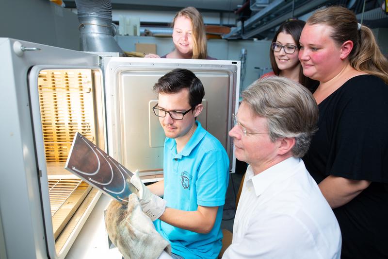 Der wissenschaftliche Mitarbeiter René Glaab zeigt Prof. Dr. Martin Müller-Roosen und seinem Team neue im Laborofen fabrizierte Testbügel.